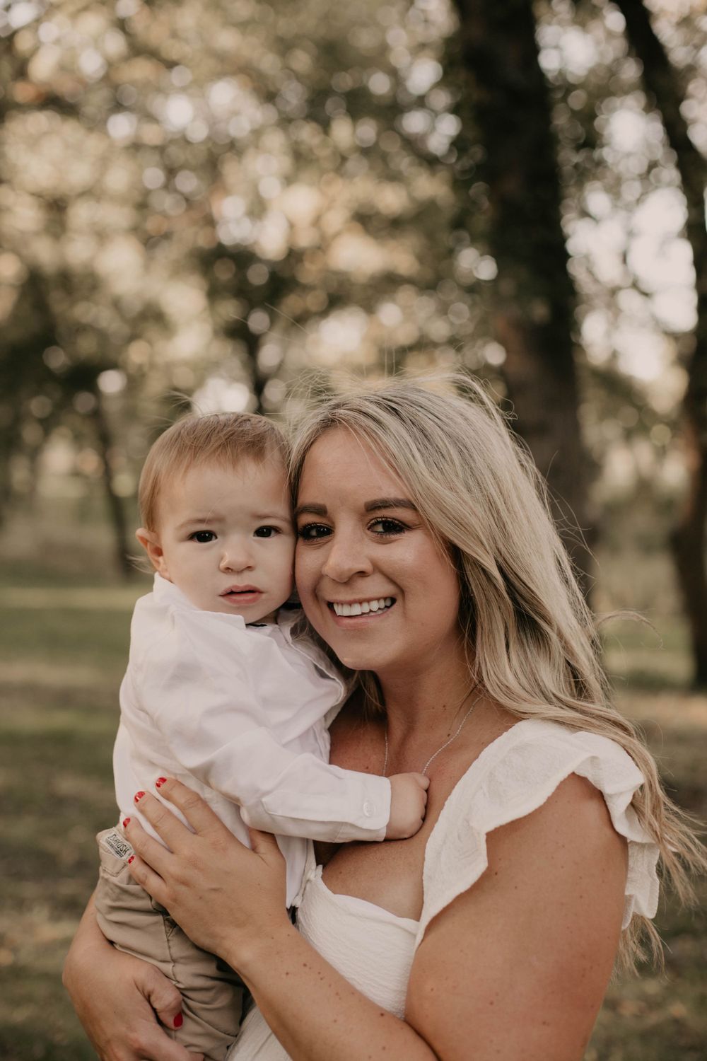 Outdoor portrait of a loving parent and young child among trees during golden hour.