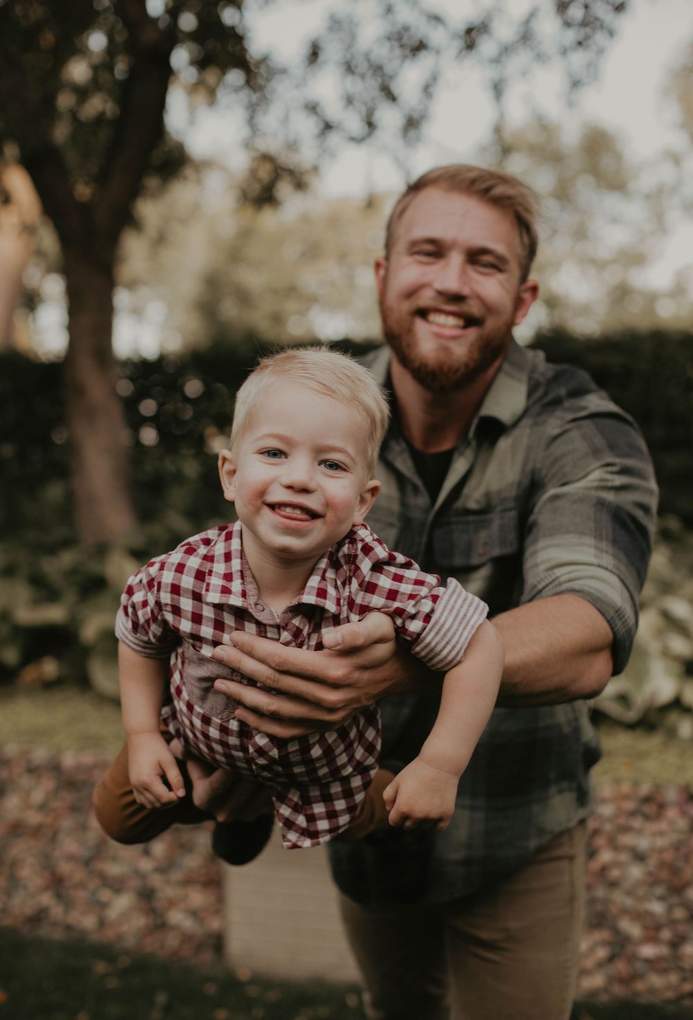 Joyful playtime moment captured outdoors with a parent lifting a small child wearing a checkered shirt.