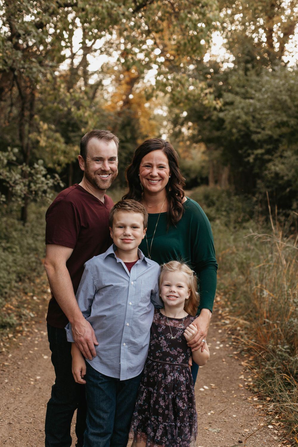 Outdoor family portrait on a wooded trail during autumn with fall foliage in the background.