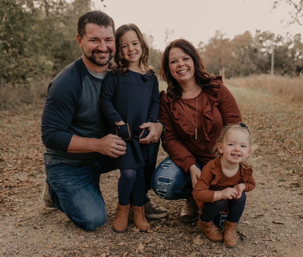 A family of four poses together on a dirt path during golden hour wearing coordinated fall outfits.