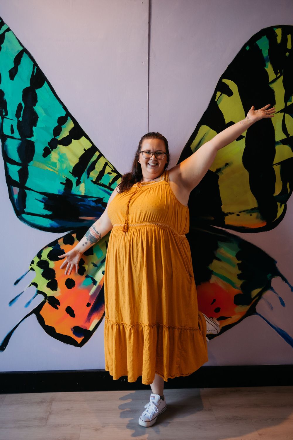 Person in yellow dress poses against colorful butterfly mural wall art.
