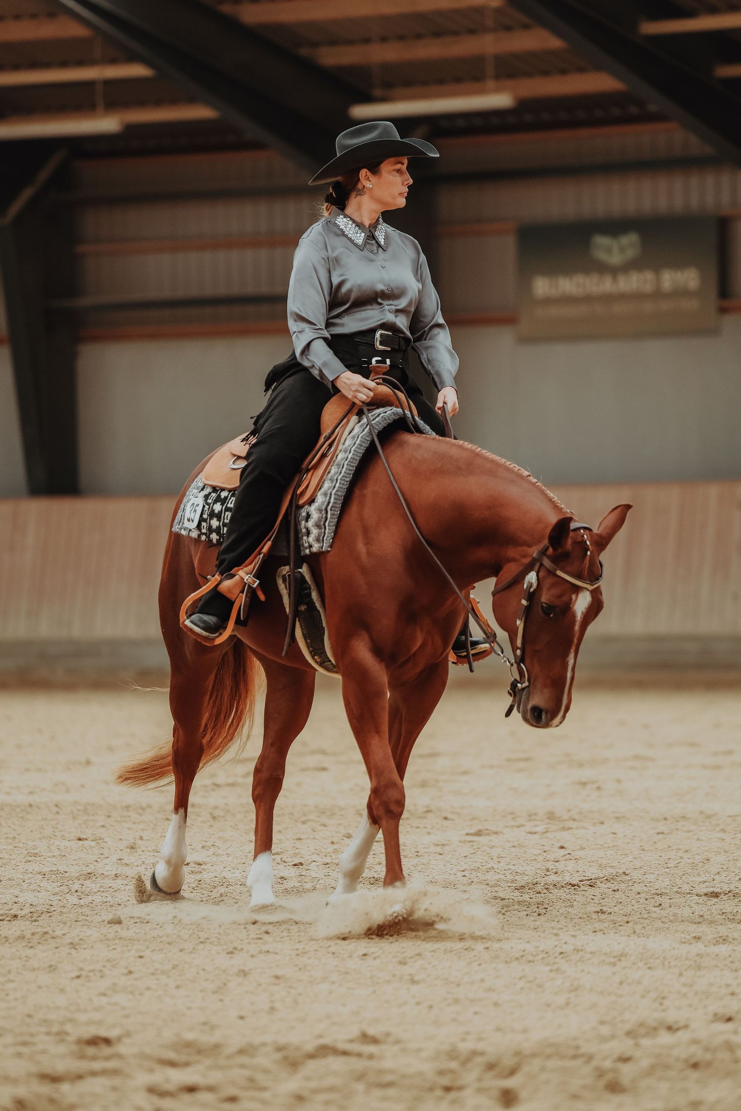 Western rider on a chestnut quarter horse practicing dressage movements indoors.