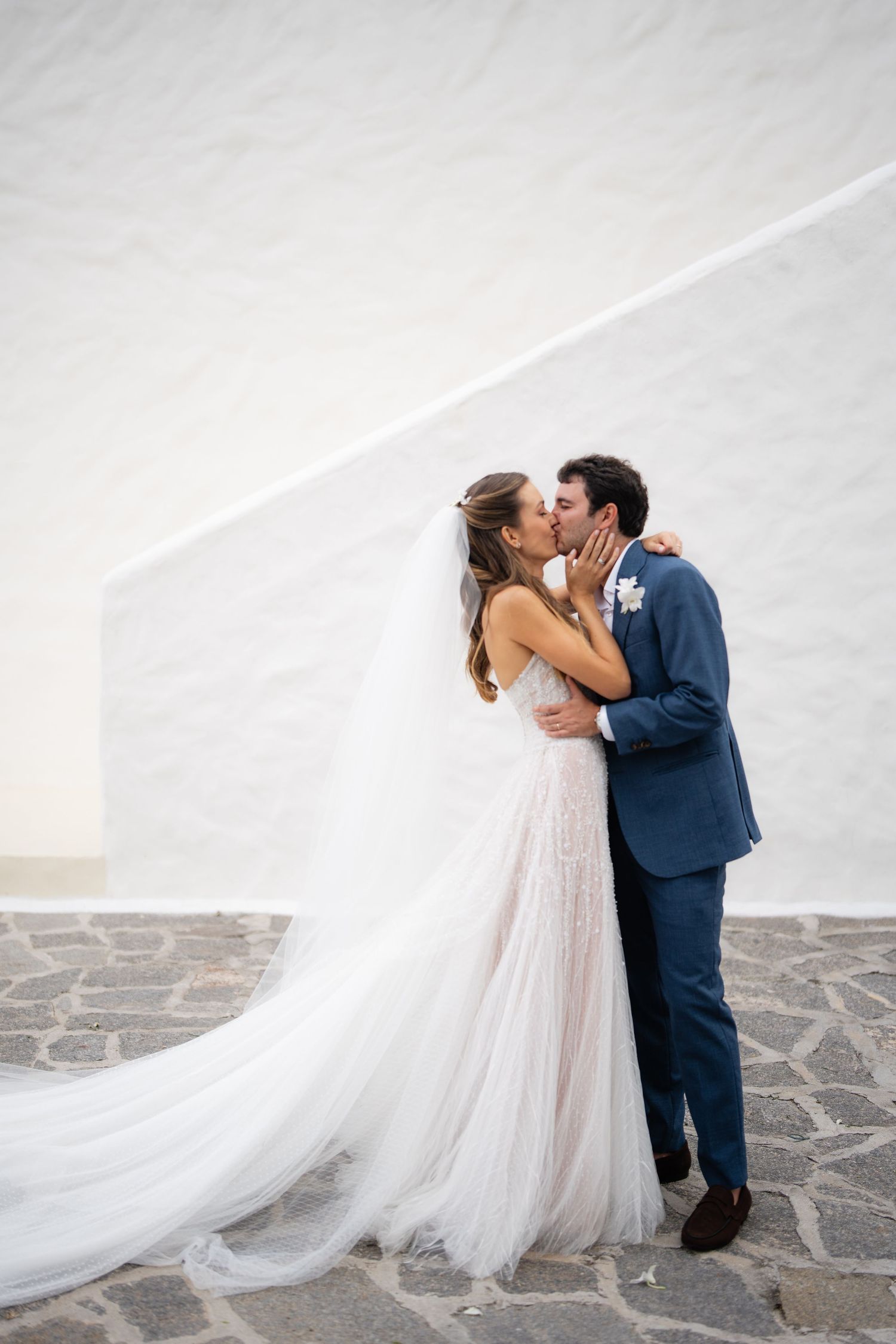 Romantic wedding moment captured against white Mediterranean architecture.