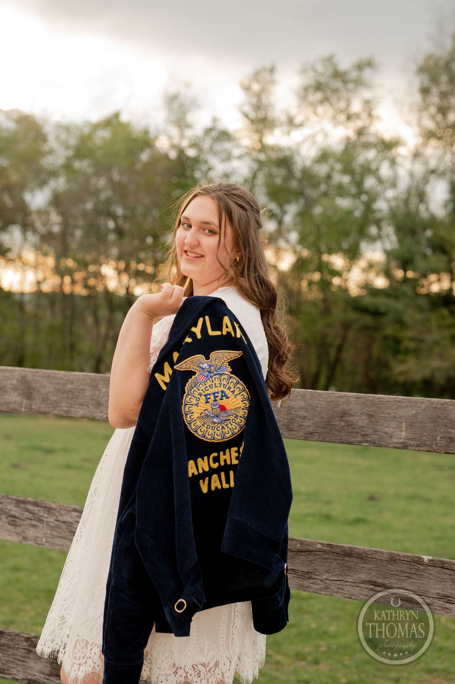 Someone poses with an FFA jacket against a wooden fence during golden hour.