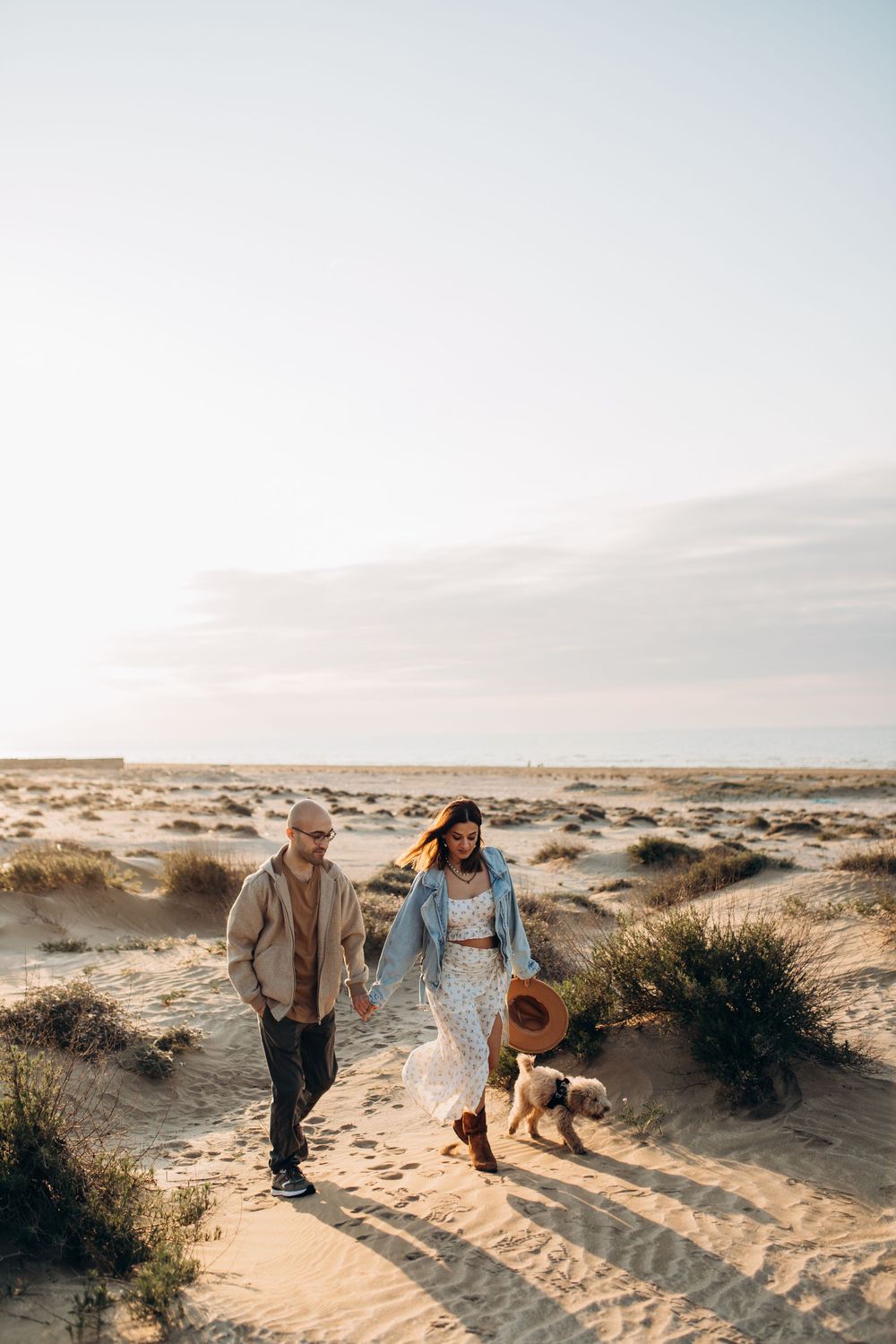 A couple and their dog explore sandy desert trails during a peaceful sunset.
