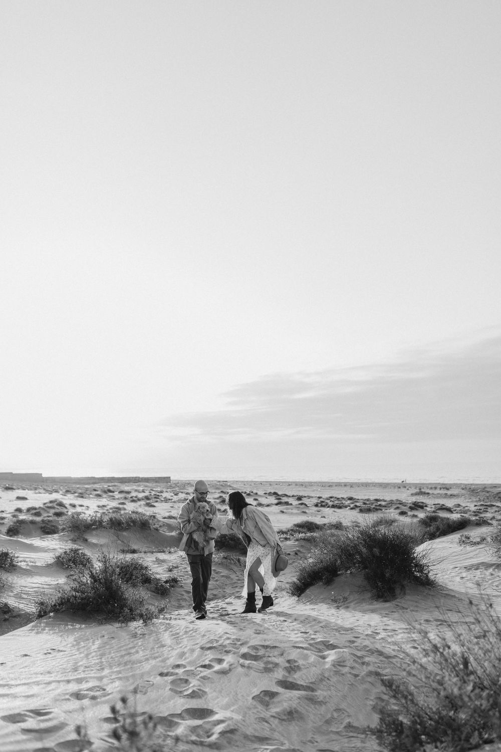 A black and white photo of a couple walking through desert landscape.