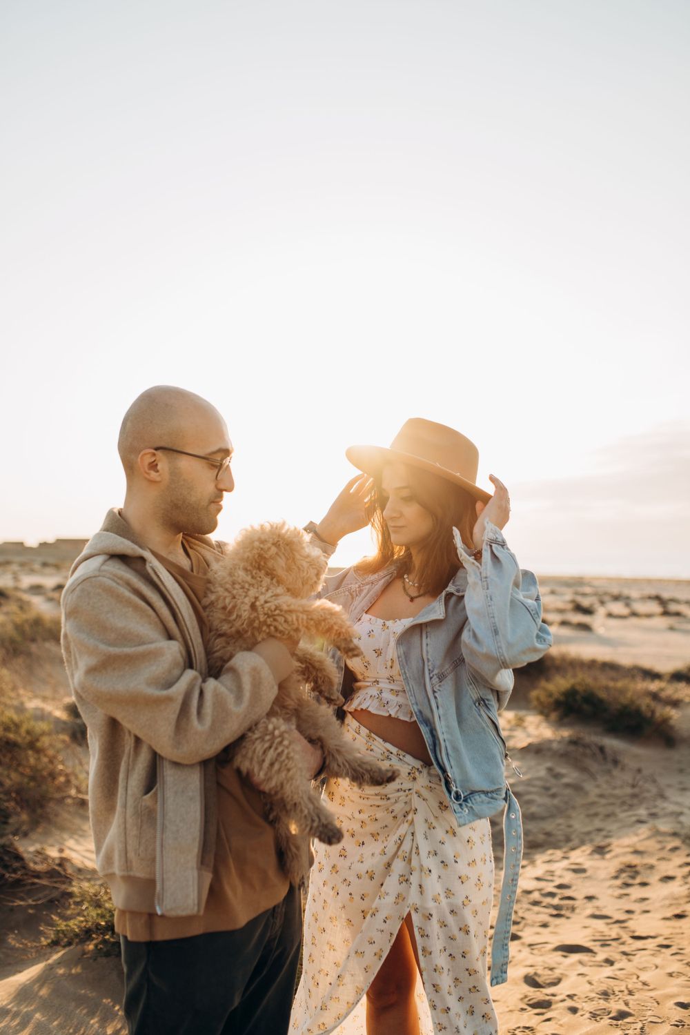 A couple in casual attire holds their fluffy pet dog while enjoying a sunny day in the desert.
