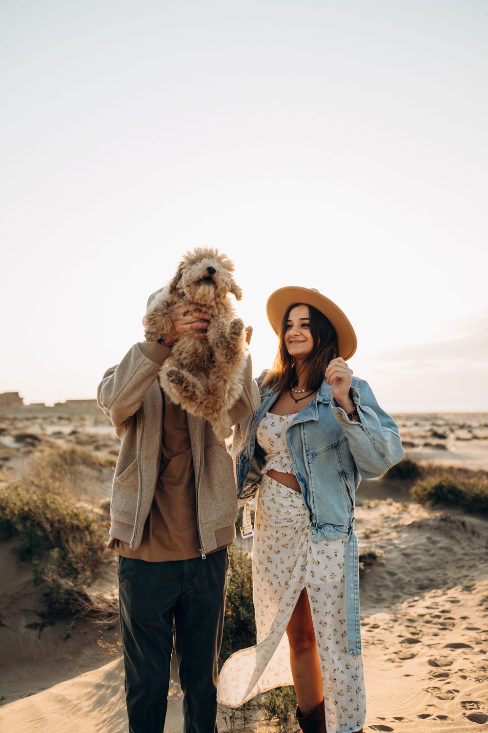 A joyful couple poses with their fluffy dog in a desert setting during sunset.
