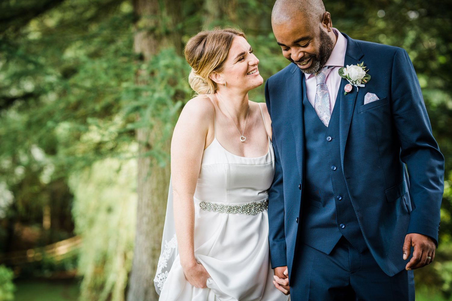 A couple in wedding attire walk through woodland after their Gretna Elopement