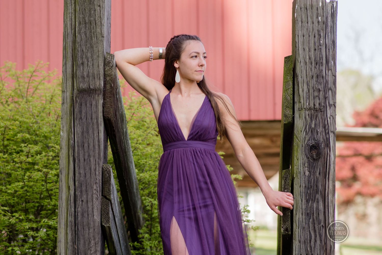 A purple formal dress creates elegant silhouette against pink barn wall and wooden posts.