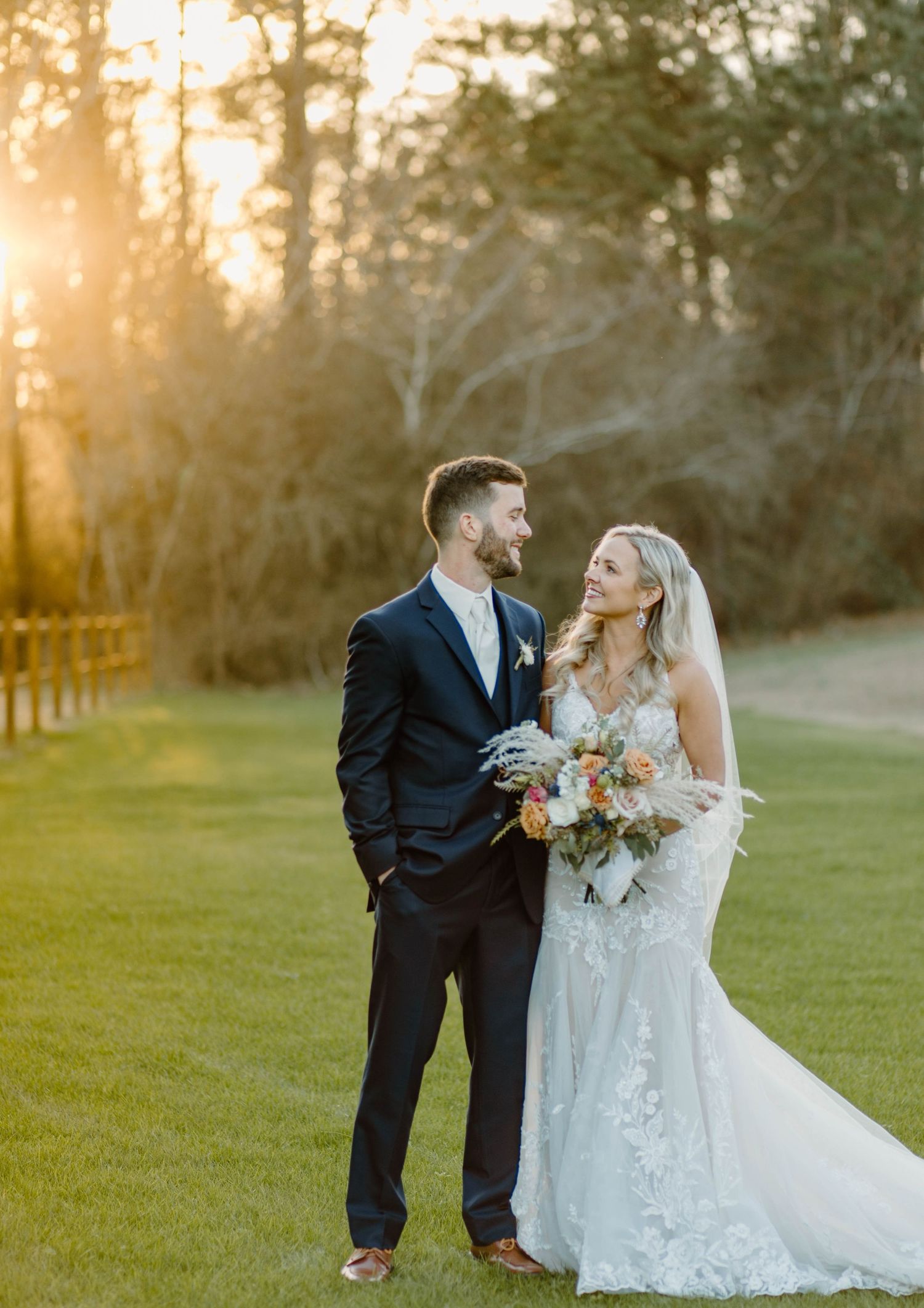 Romantic sunset wedding portrait with couple on lush green lawn.