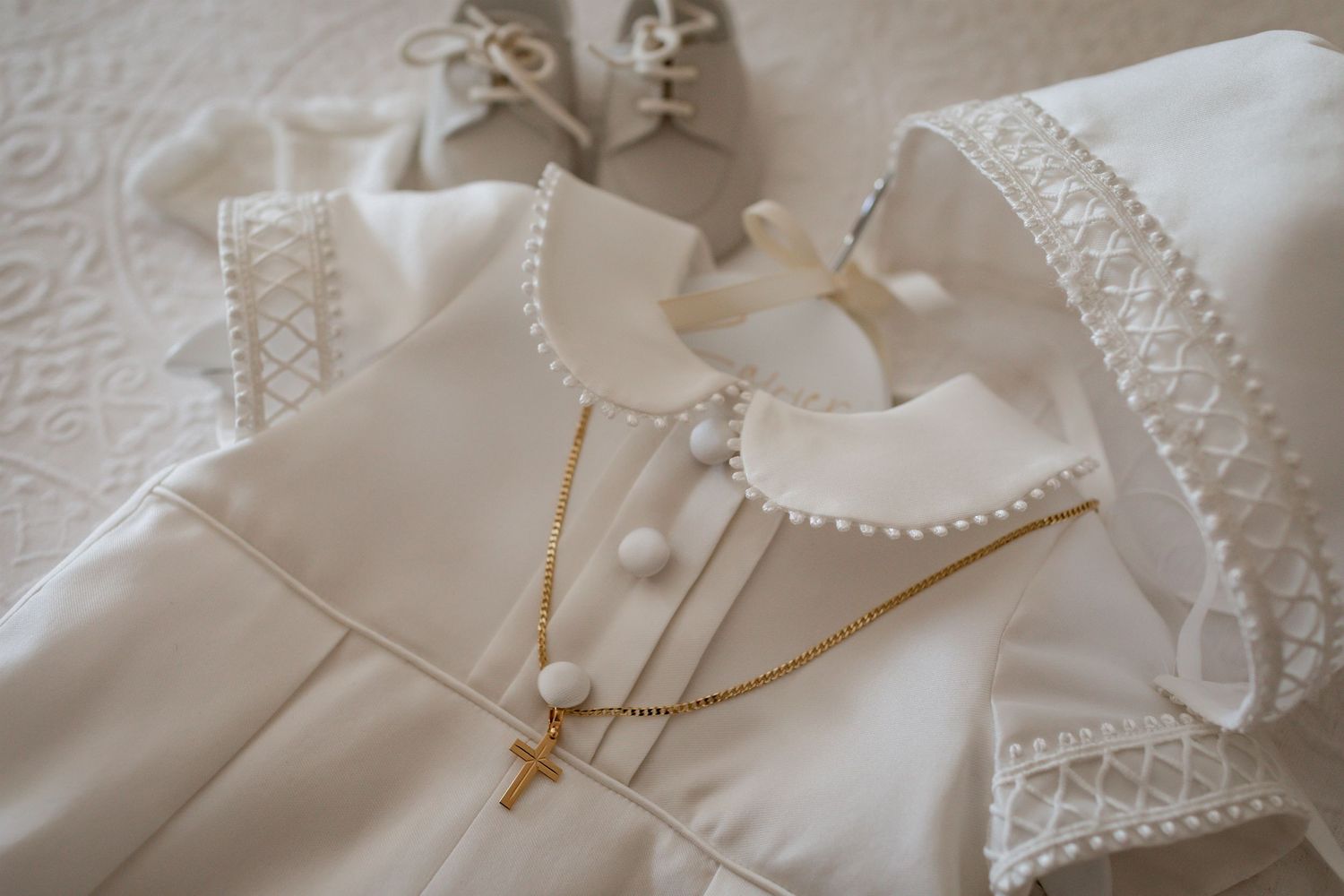 White christening or baptism gown with delicate lace trim and gold cross necklace detail.