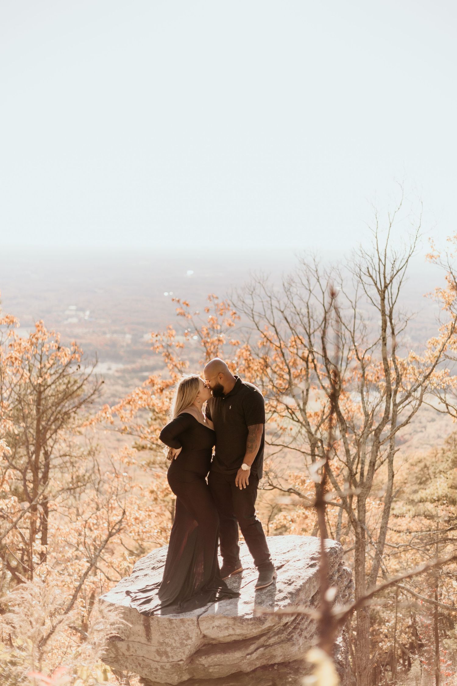 Romantic silhouette of couple embracing on mountain overlook during sunset.