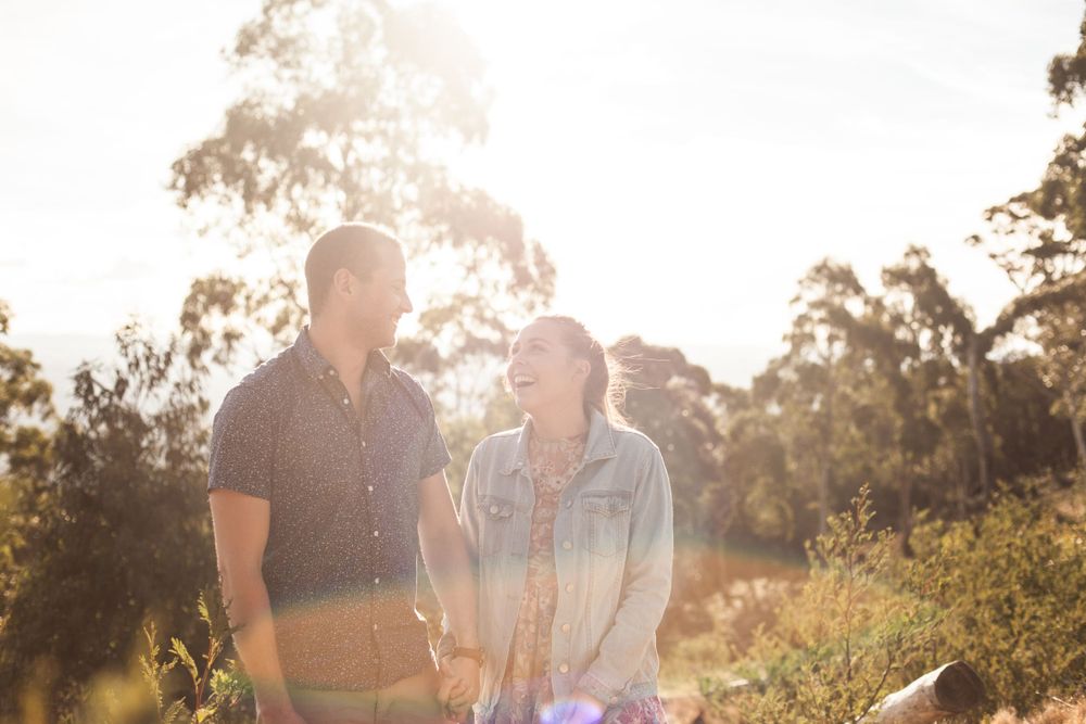 Couple walking together in golden sunlight through a natural outdoor setting during their engagement session.