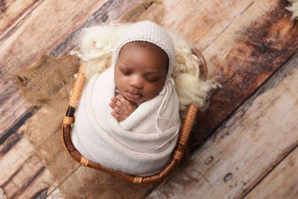Peaceful newborn wrapped in white blanket sleeping in woven basket on wooden floor.
