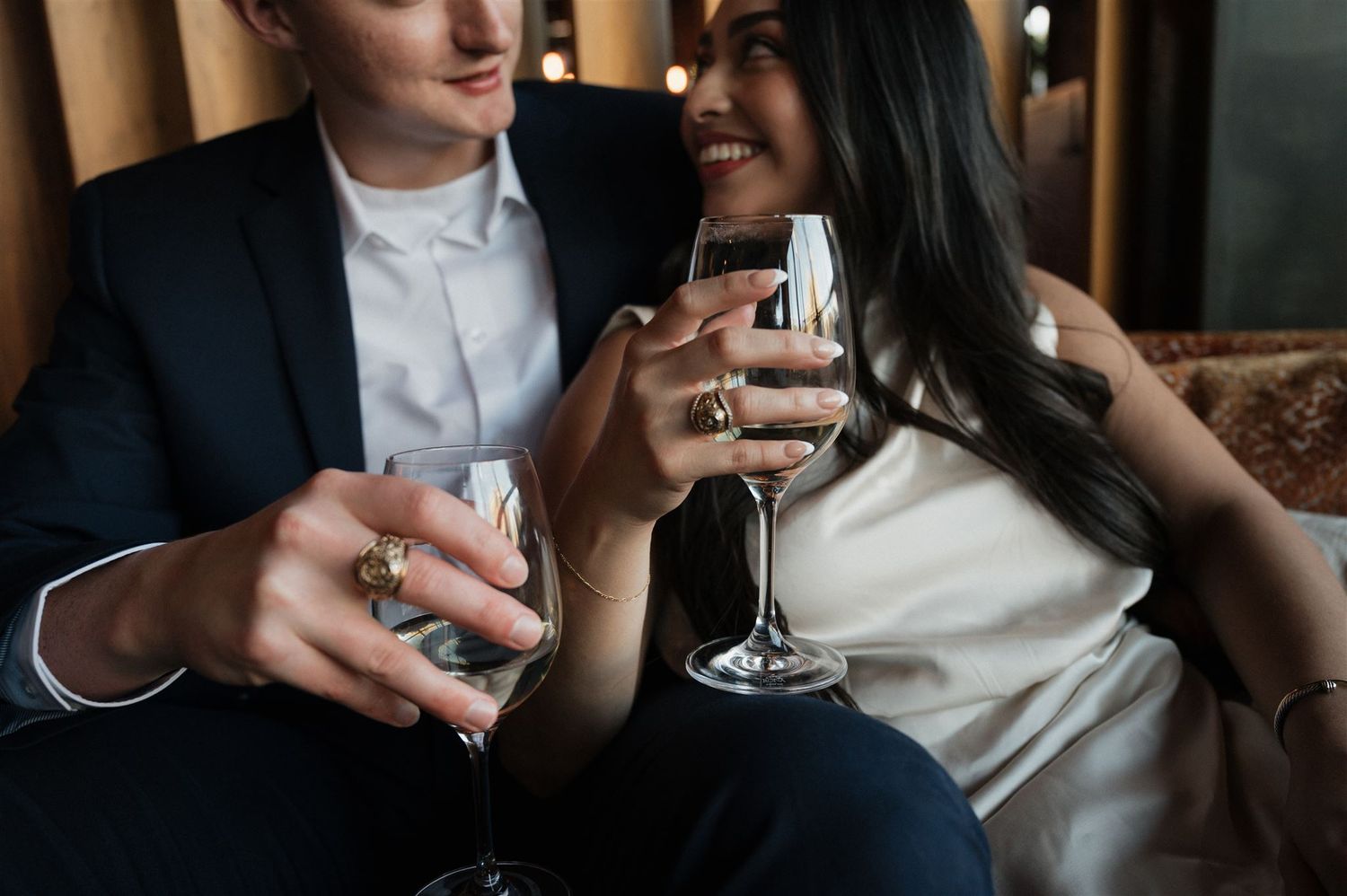 A couple shares wine glasses while sitting intimately on a leather couch.