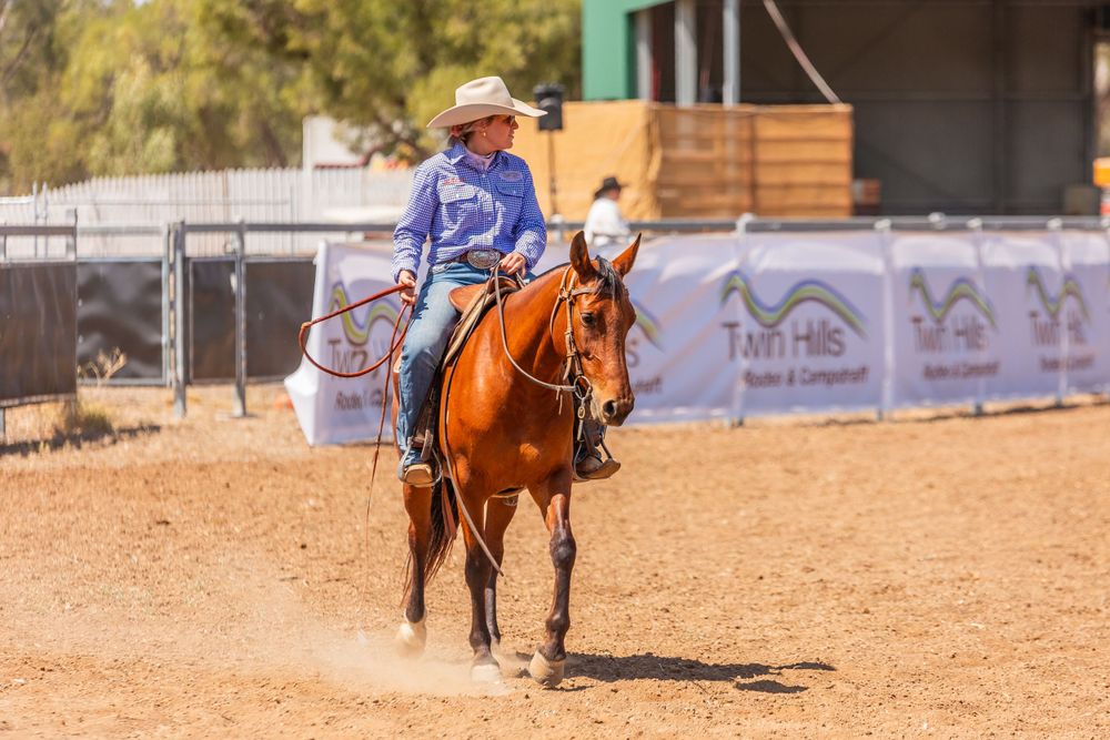 A chestnut horse and rider compete in a western riding event in a dusty arena.