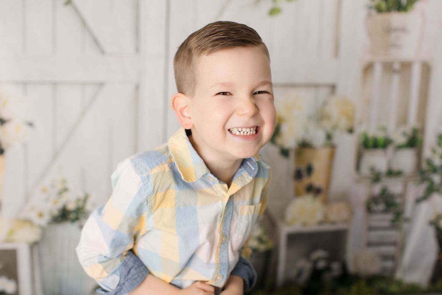 Young child laughing joyfully in patterned shirt against white background.