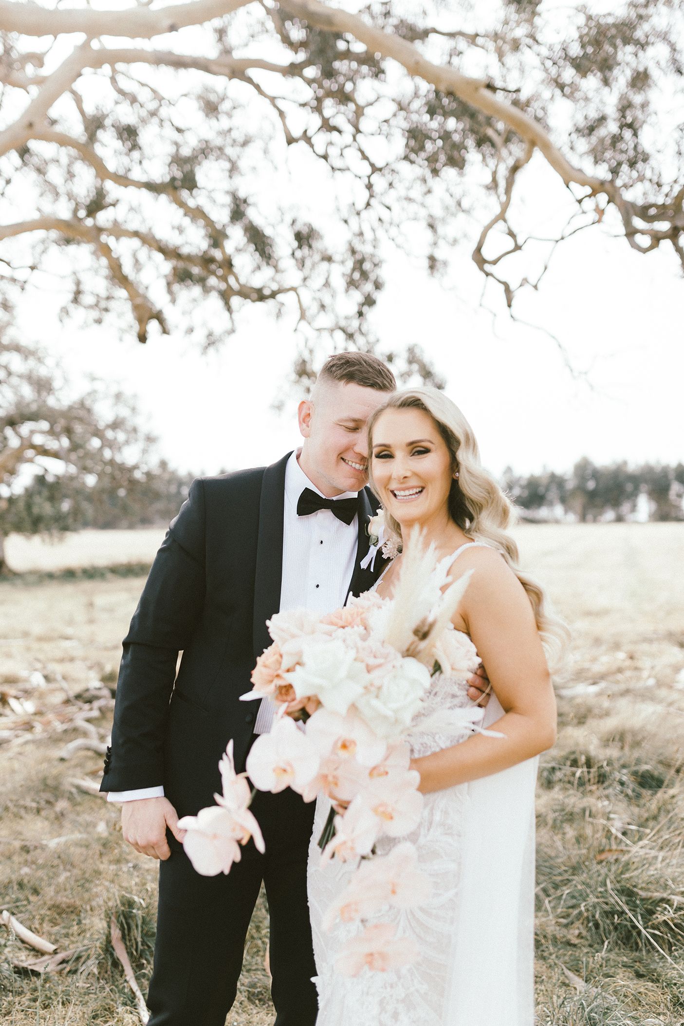 Romantic wedding photography featuring a couple with beautiful orchid bouquet under tree branches.