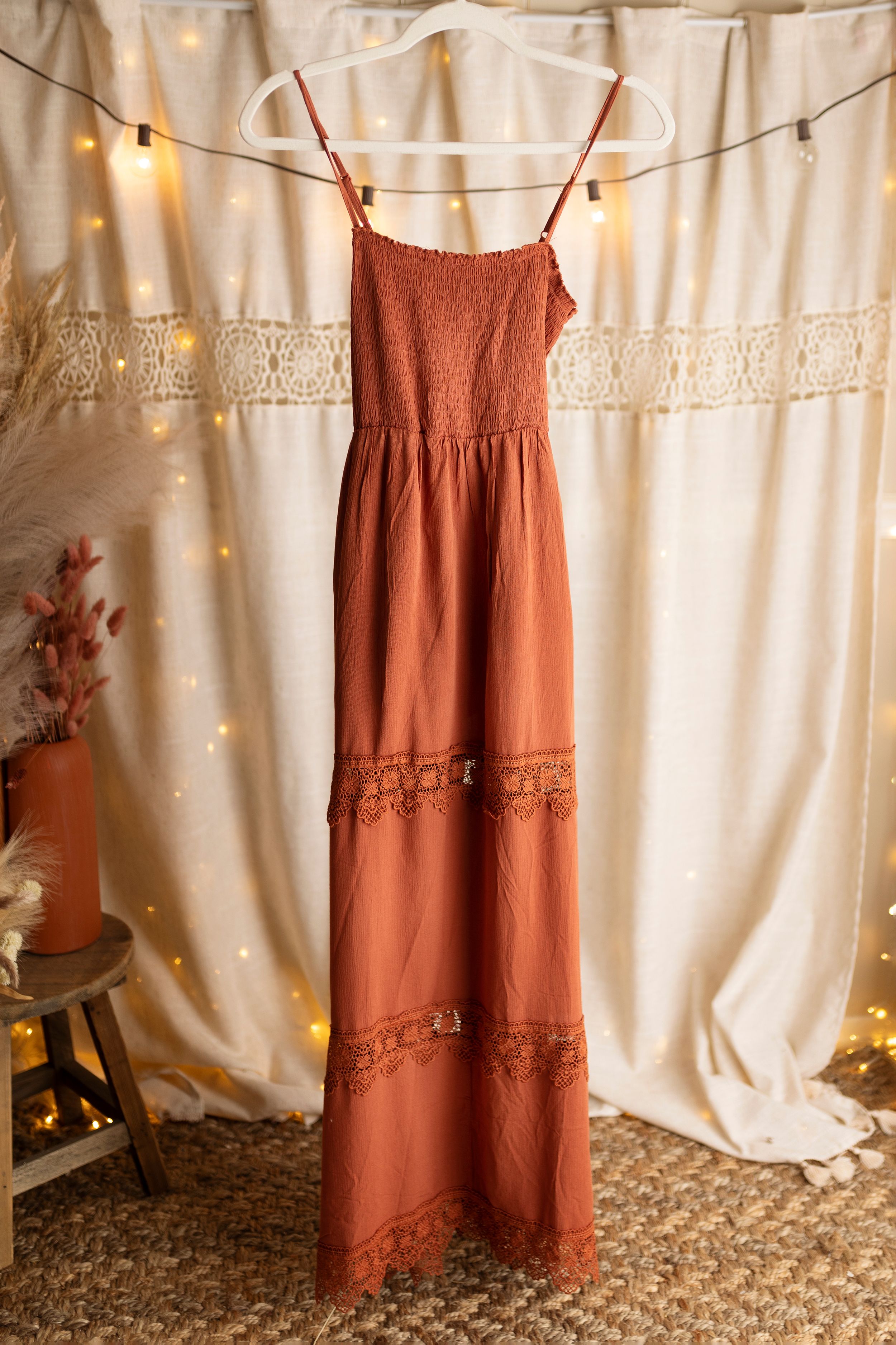 Rust-colored summer dresses with lace details hanging against a white backdrop with string lights.