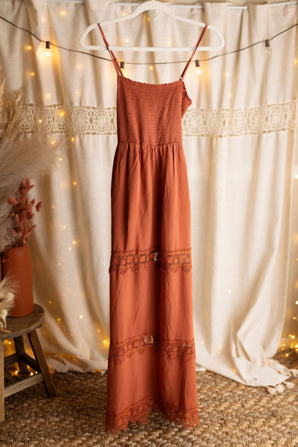 Rust-colored summer dresses with lace details hanging against a white backdrop with string lights.