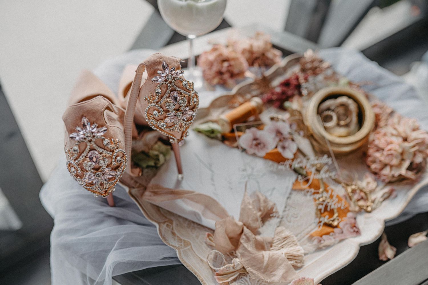 Elegant flat lay of rose gold bridal accessories including jeweled bouquet wrap, dried florals, and rings on marble.