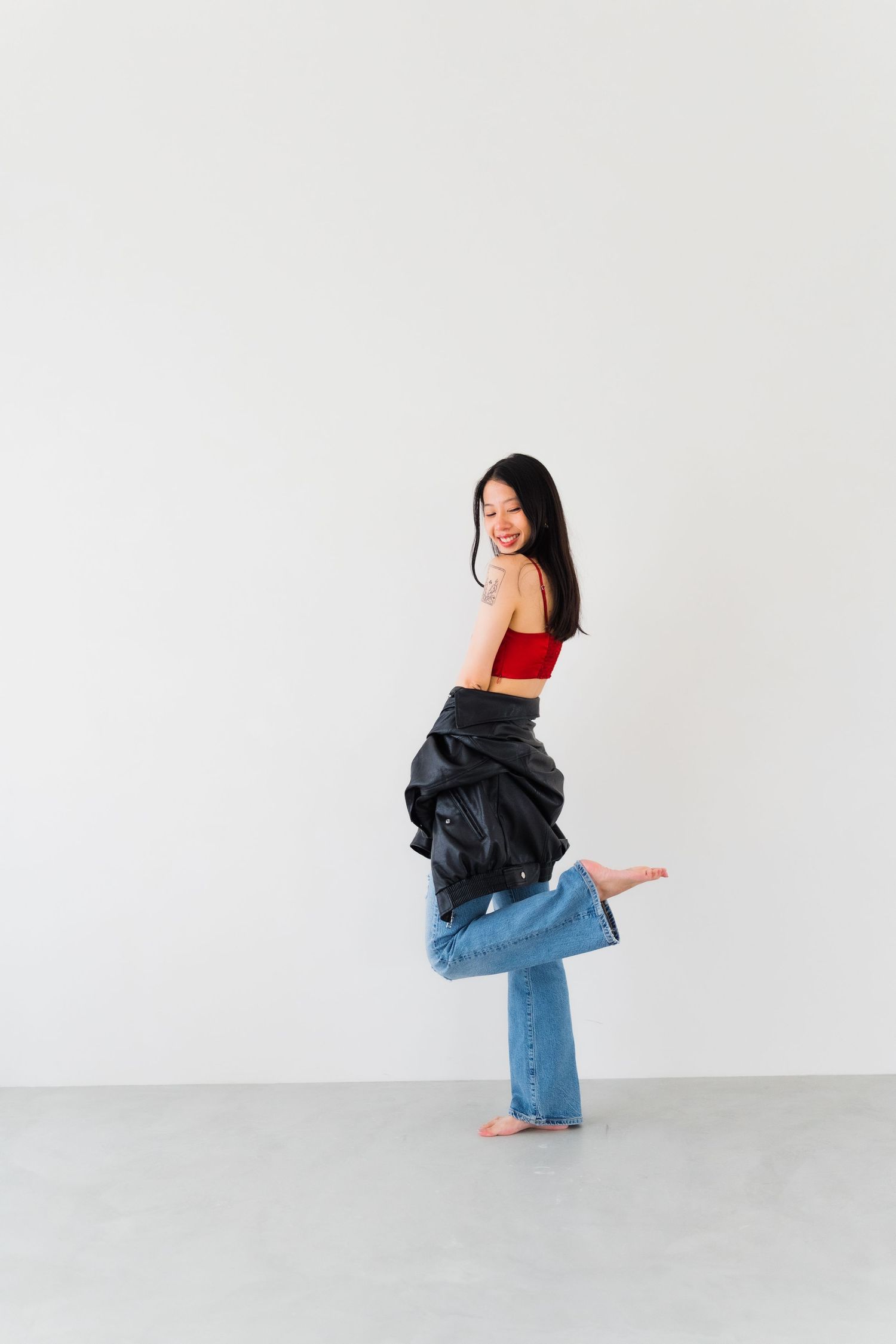 Woman in red crop top and jeans strikes playful pose against white studio background.