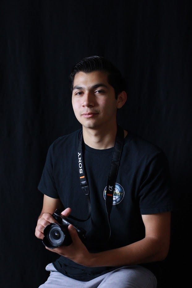 Young male photographer holding a Sony camera against a dark studio background.