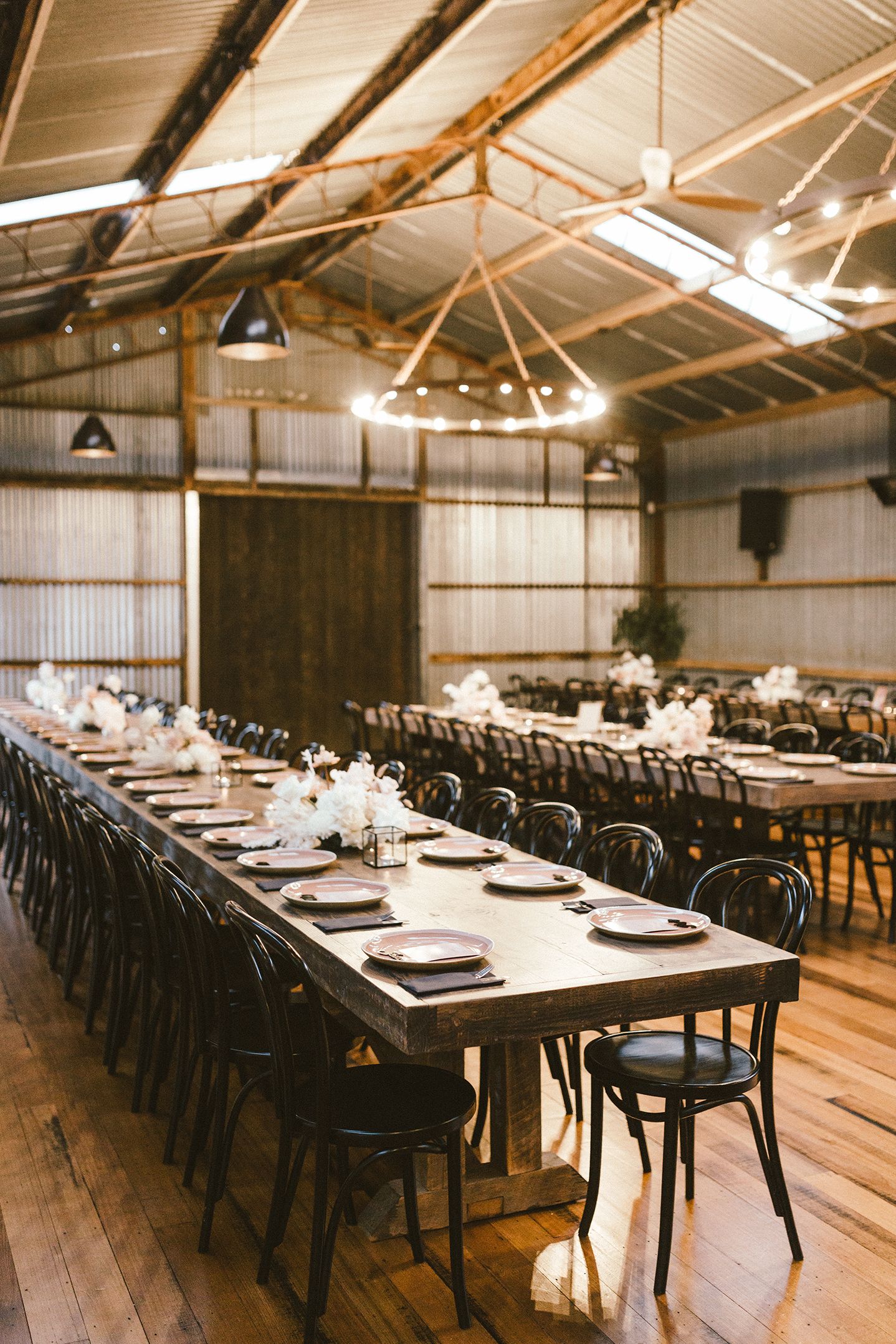 Rustic barn wedding venue with long tables and string lights hanging from wooden beams.