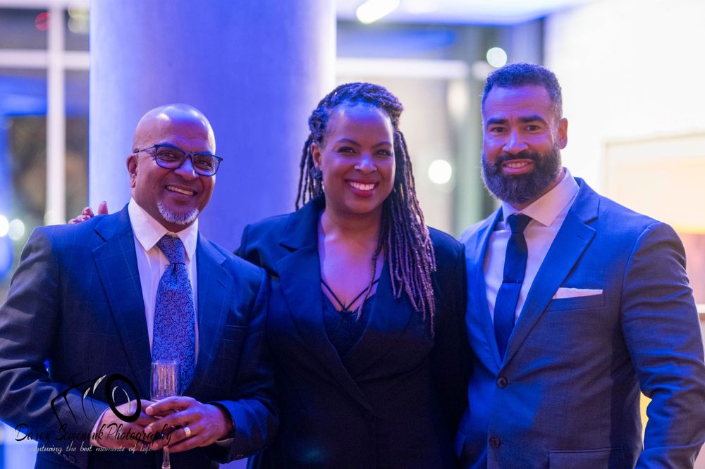 People in formal business attire gathered at an event with blue lighting.