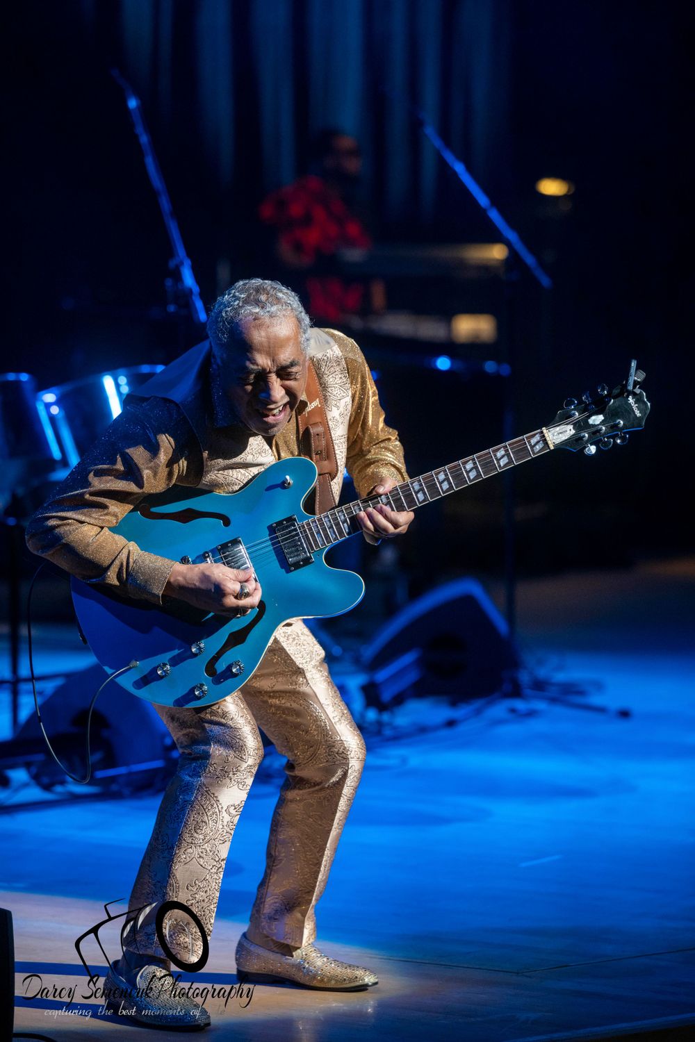 Guitarist performing on stage under dramatic blue lighting during a concert performance.