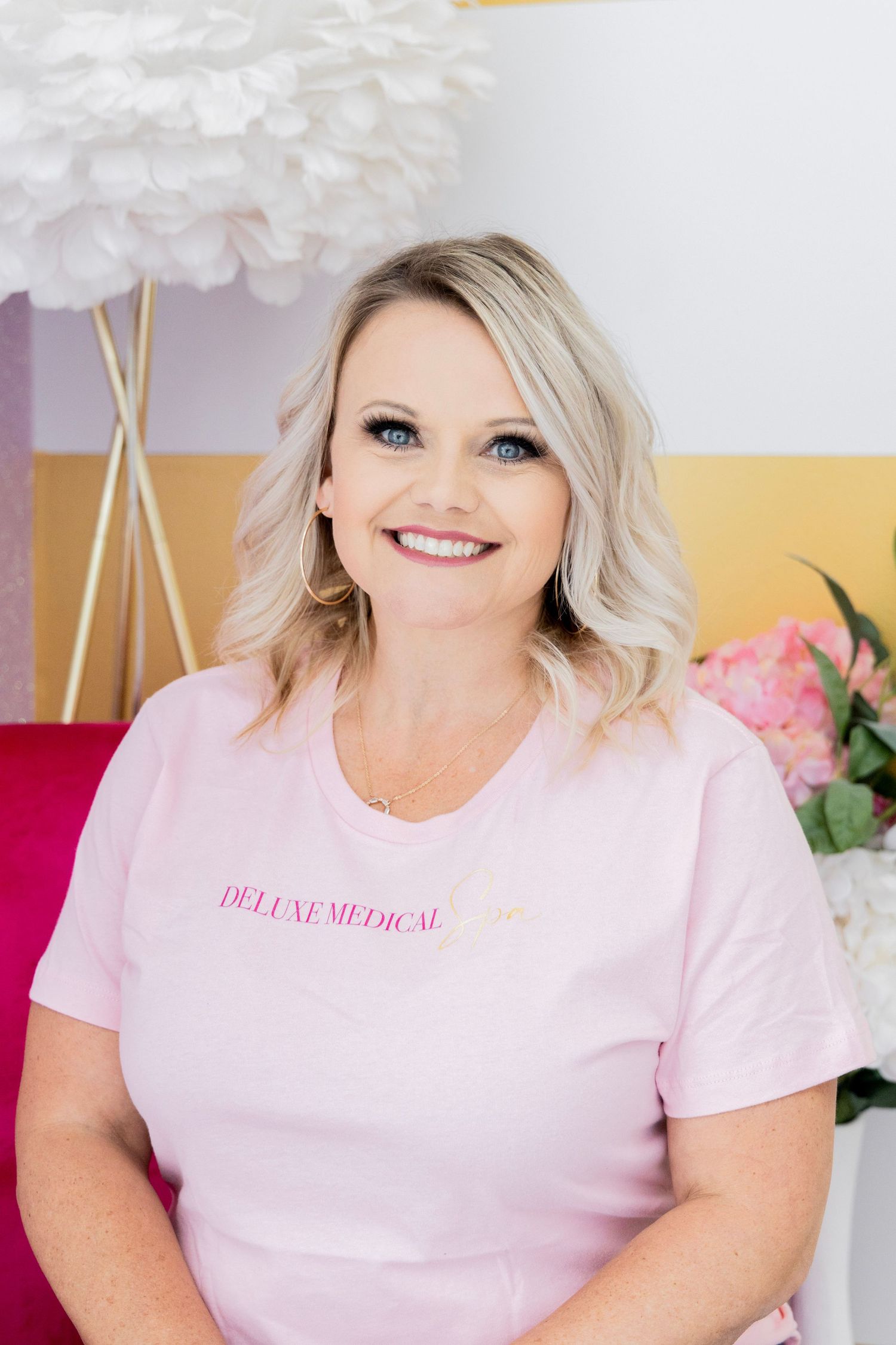 Person in pink t-shirt with text sitting on pink chair with decorative backdrop.