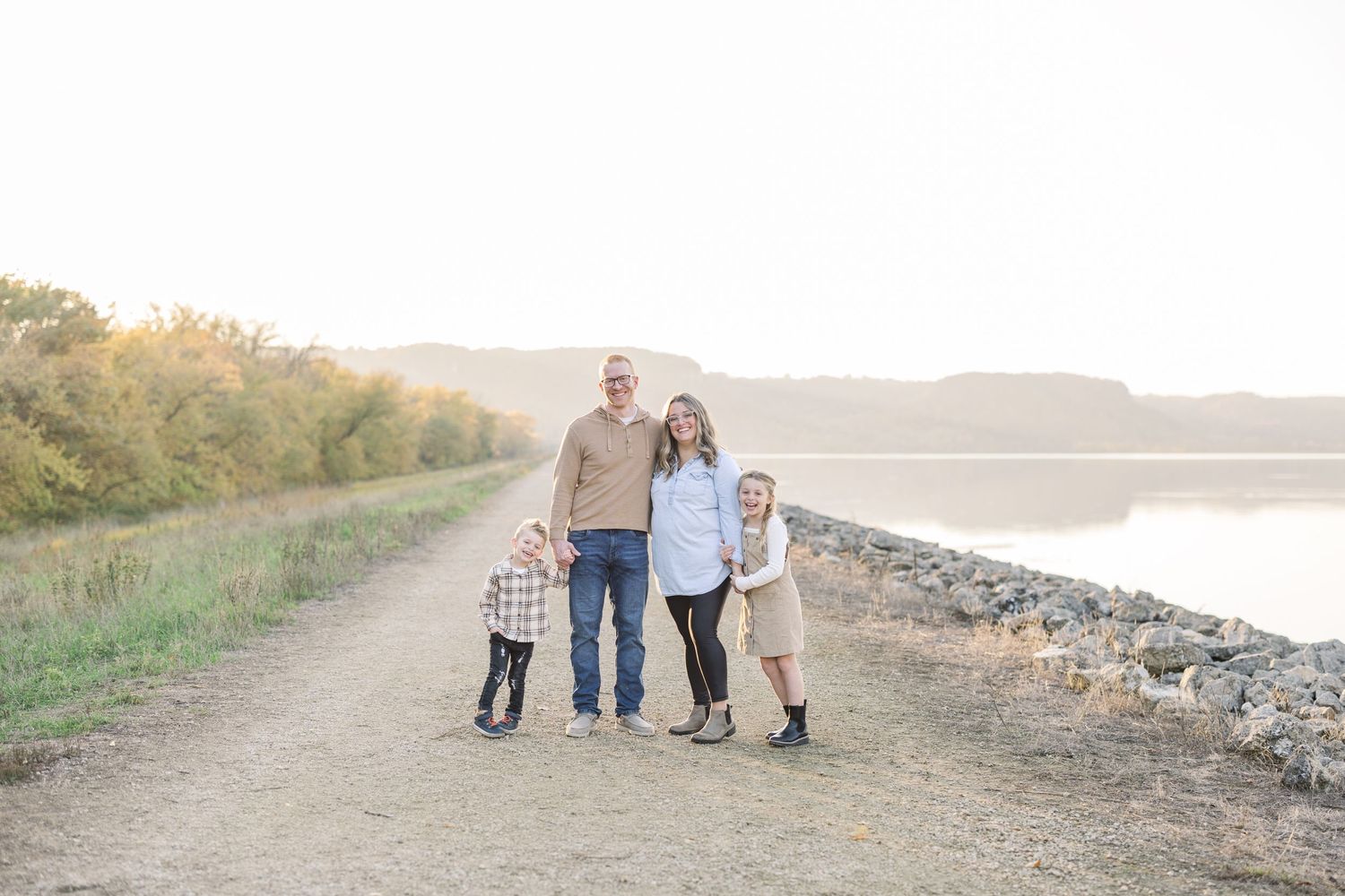 A family of four walks together along a waterfront path during sunset.