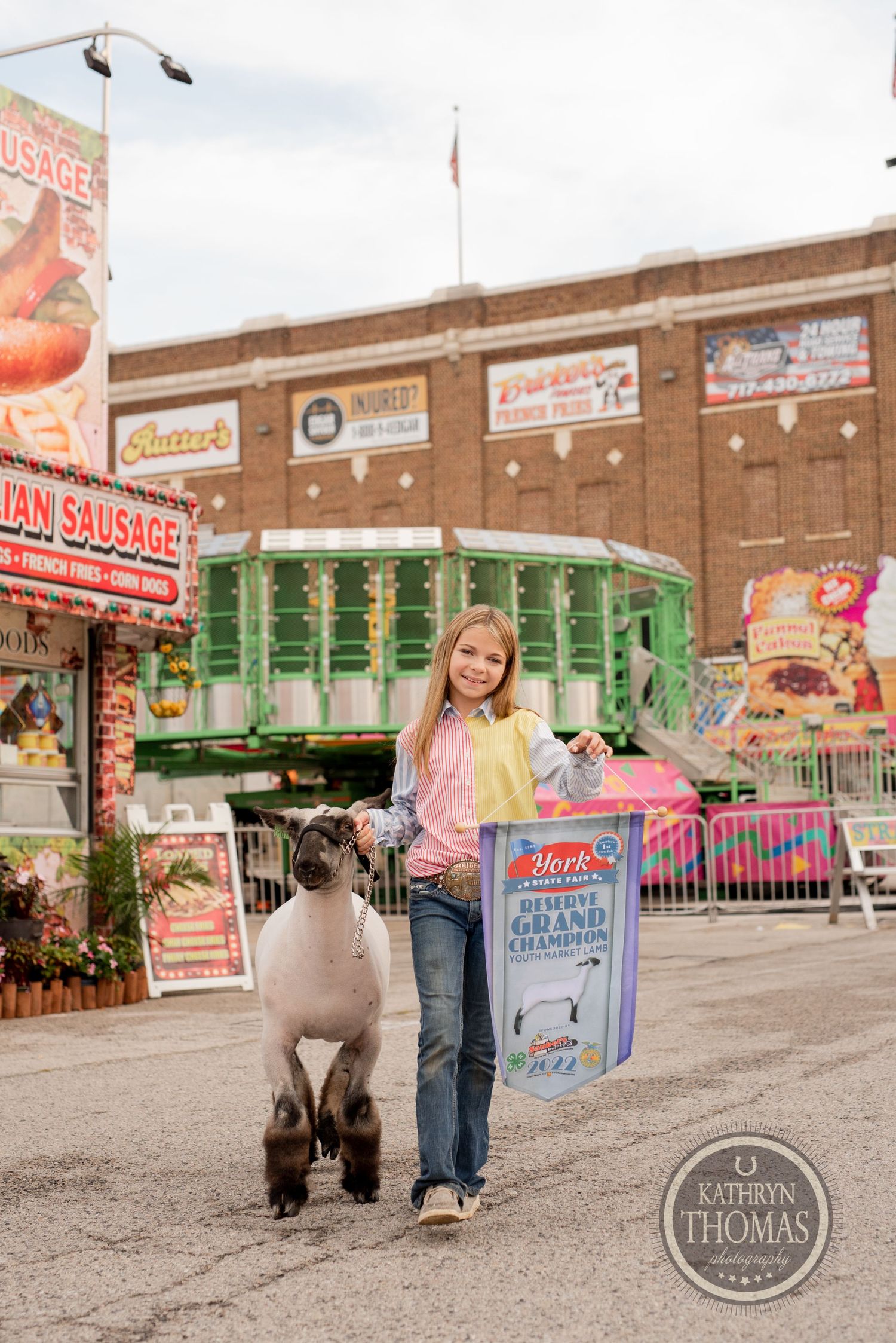 A show sheep and handler pose by carnival food stands and rides at the York Fair.