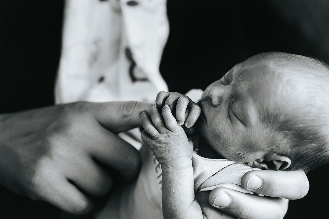 Teeny, tiny newborn twin holds the giant finger of their parent.