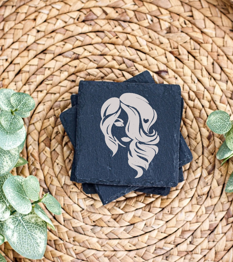 Elegant female silhouette logo design on black slate coasters with green leaves on woven placemat.