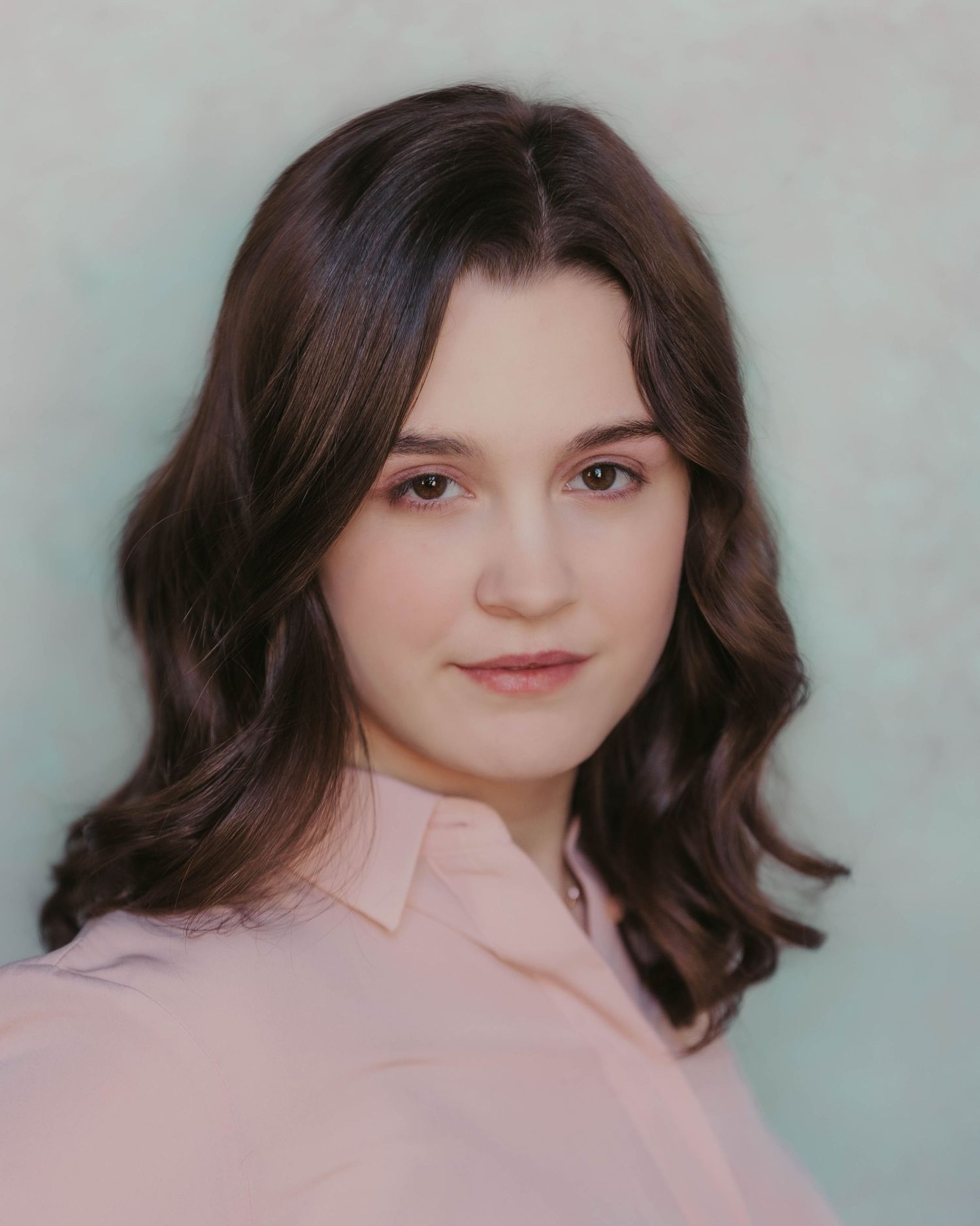 Portrait against light background featuring soft waves and pink collared blouse.