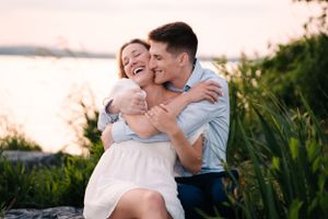 A couple shares a tender embrace while sitting on rocks by the water at sunset.