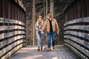 Casual couple strolling across a wooden bridge in a wooded area during autumn.