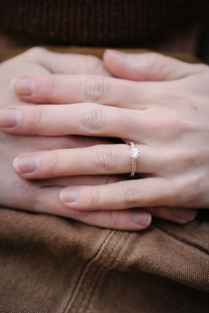 Close-up of hands resting on brown fabric with a sparkling engagement ring.