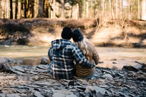 A couple sitting together on rocky terrain with sunlit forest in the background.