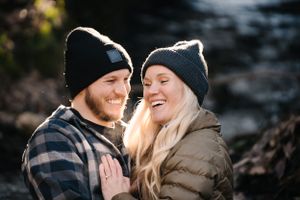 A couple laughing together while wearing matching winter beanies in an outdoor setting.