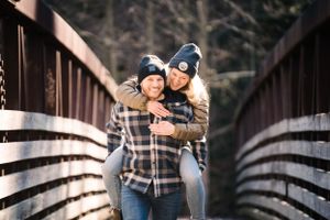 A couple sharing a playful embrace on a wooden bridge surrounded by nature.