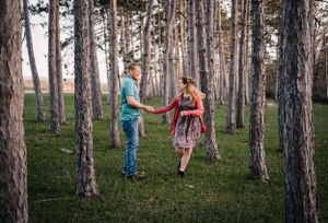 A romantic couple playfully walking through a pine forest holding hands.