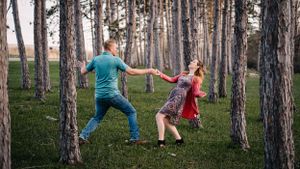 A playful couple dancing between tall pine trees in a forest setting.