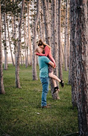 A romantic embrace between a couple surrounded by tall pine trees in a forest.