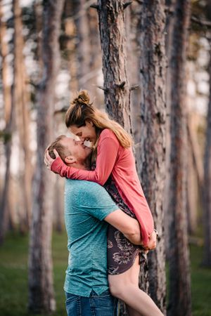 A romantic couple sharing an intimate moment among pine trees at sunset.