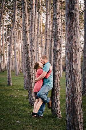 Romantic couple embracing against a tall pine tree in a serene forest setting.