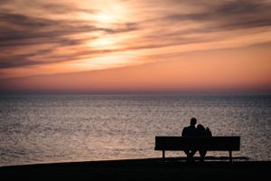 Silhouette of couple sitting on bench watching beautiful ocean sunset.