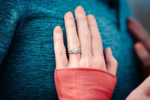 Close-up of a sparkling engagement ring on a woman's hand wearing a coral colored sleeve.